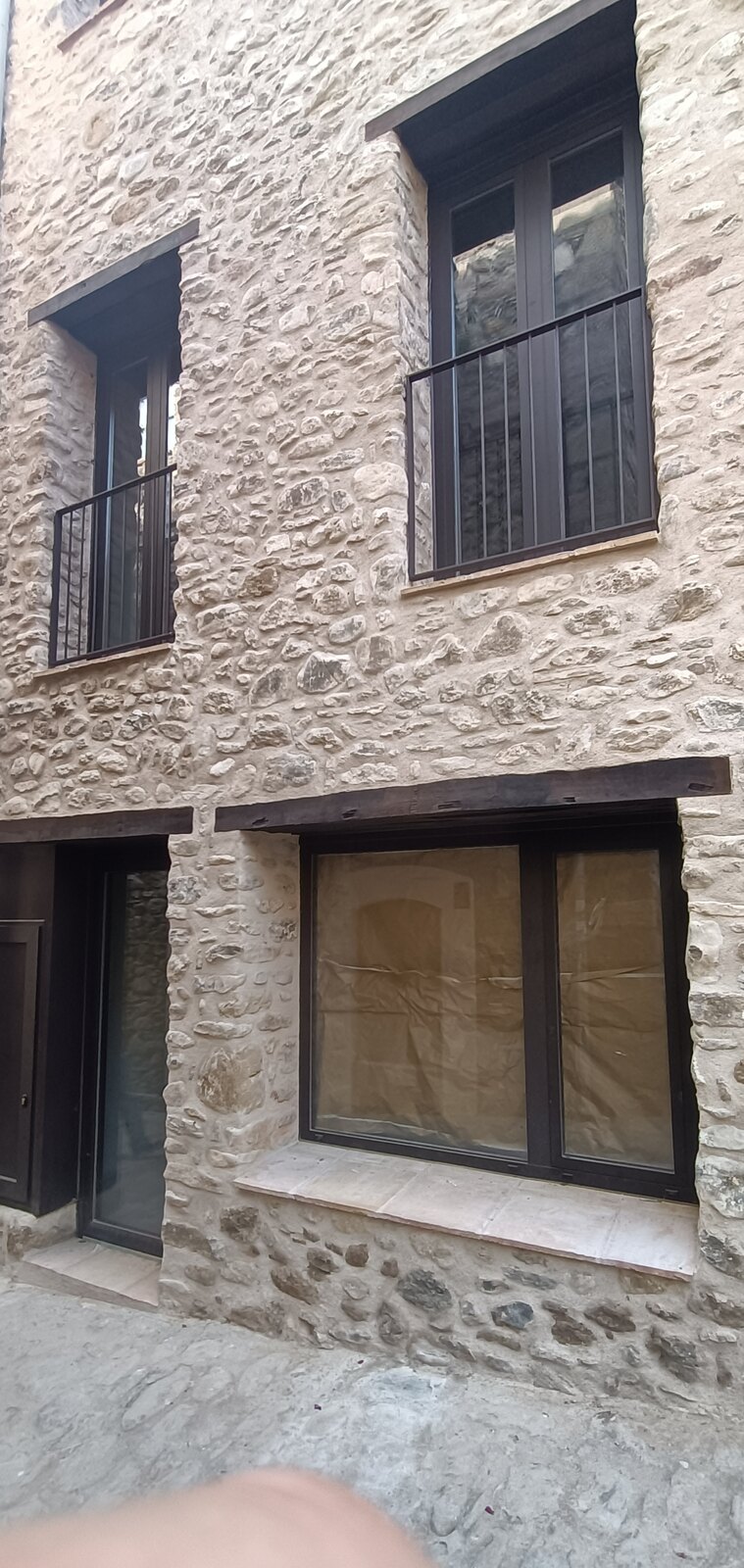 Fachada de piedra restaurada con la carpintería nueva instalada, en Mieres